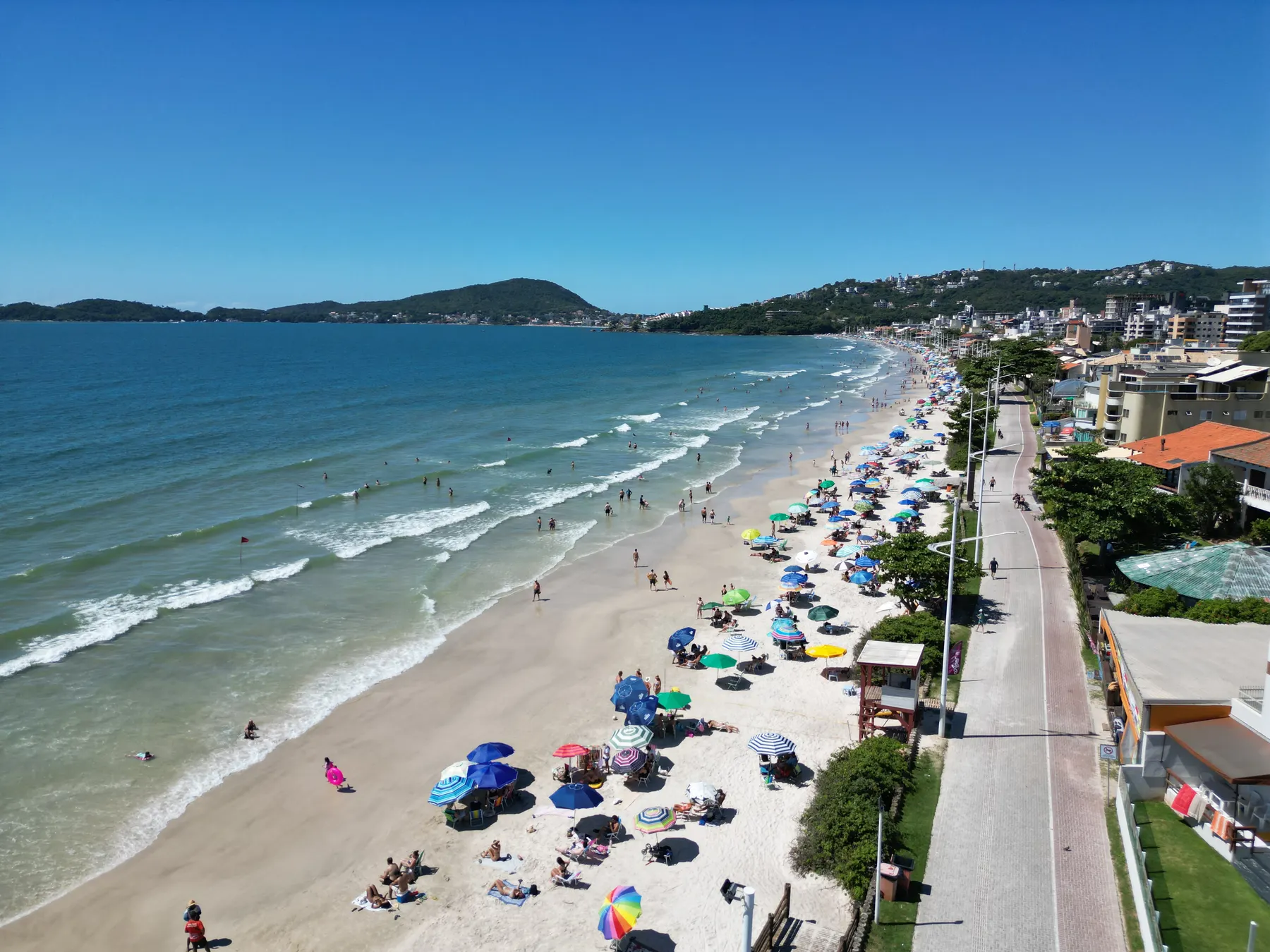 Praia de Bombas em dia de sol, com guarda-sóis coloridos e mar calmo, em Bombinhas - SC
